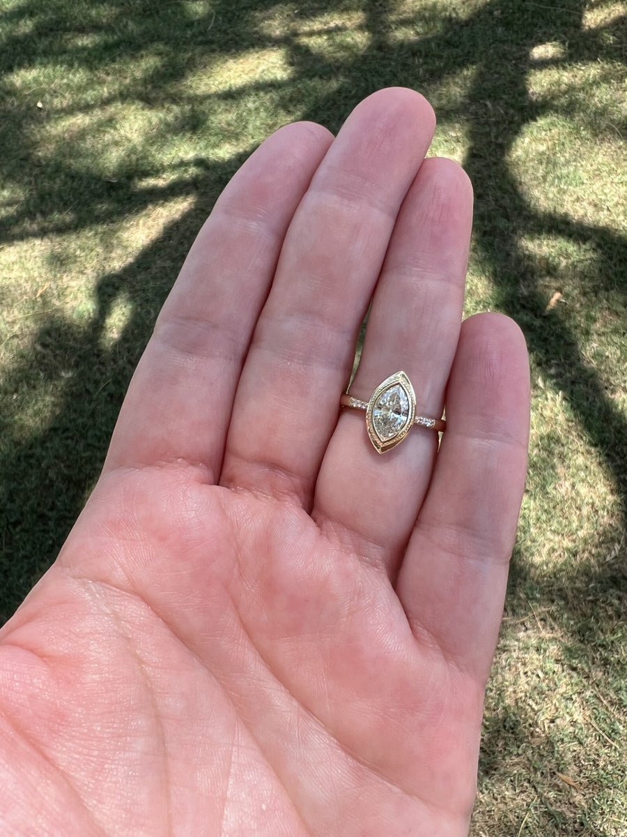 Bezel set diamond marquise ring with miligrain around the diamond and diamond accents down the shank placed on ring finger